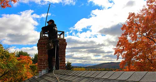 Chimney Sweep tech with safety gear fall trees and beautiful blue sky with clouds