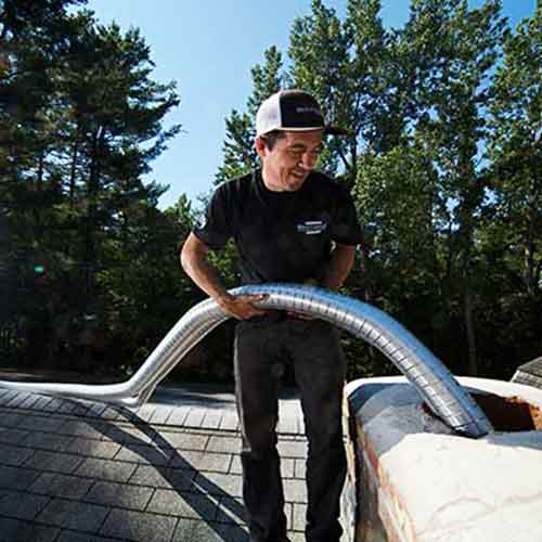 Man feeding liner down chimney standing on a roof wearing shirt and hat with Brickliners logo