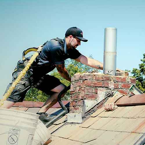 Brickliners tech on roof with safety equipment rebuilding chimney