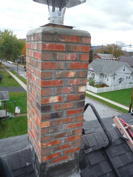 Chimney Repair After-all tuckpointing complete new flashing, new crown and cap, ladder to the right and subdivision in background