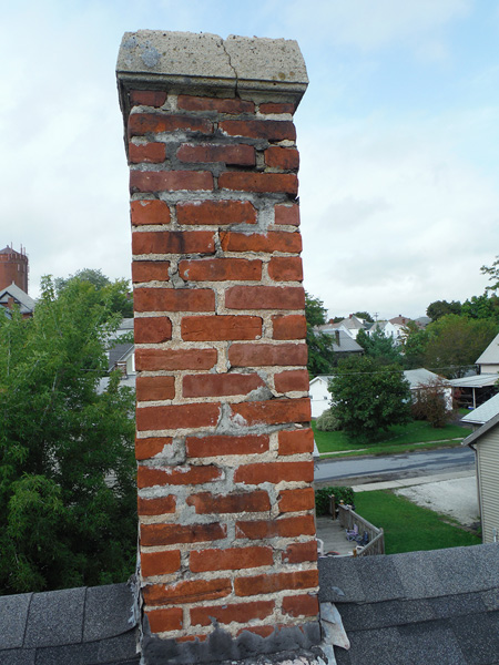 Chimney has cracks throughout spalling, needs new flashing, crown has a very large crack homes in background