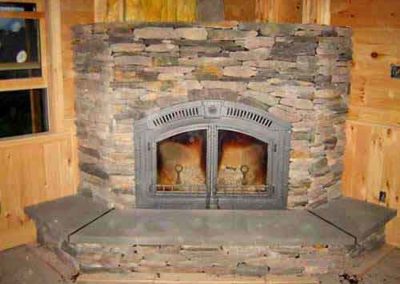 Cultured Stone corner wood burning fireplace with built up hearth and wood on the walls