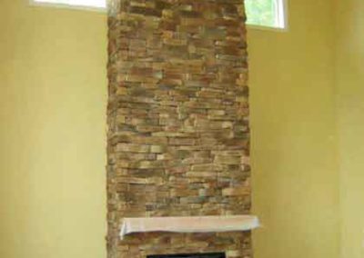 Cultured Stone fireplace that goes up to the ceiling with a window on each side at the top and black insert