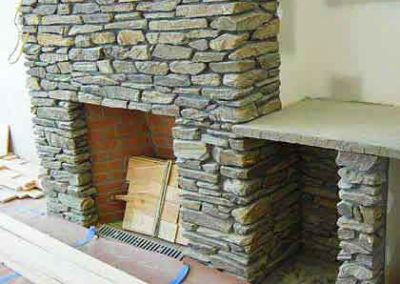 Stacked stone fireplace with wood storage to the right 2x6 planks on floor still under construction