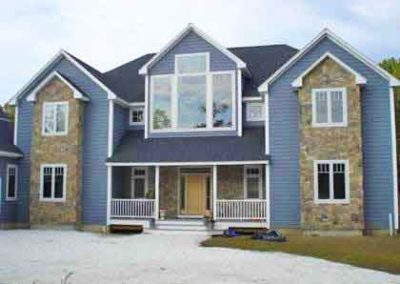 Stone Facade on each side of 2 story blue vinyl home with small porch-2nd story has a wall of windows