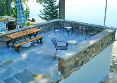 Stone Patio Restoration overlooking lake has picnic table and iron chair with work truck to the left